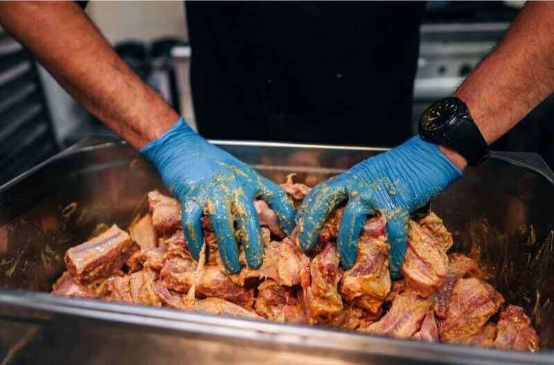 A chef is marinating beef cubes in a large pot.