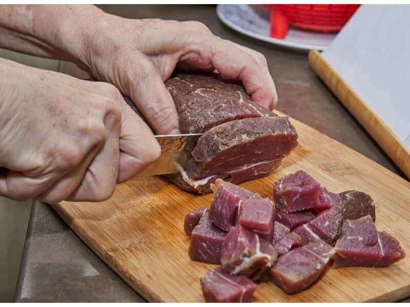 A man is cutting beef into cubes like a pro.