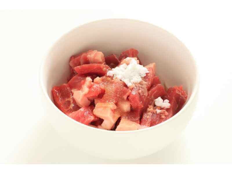 Seasoning the beef cubes with salt, pepper, flour, and smoked paprika in a white bowl.