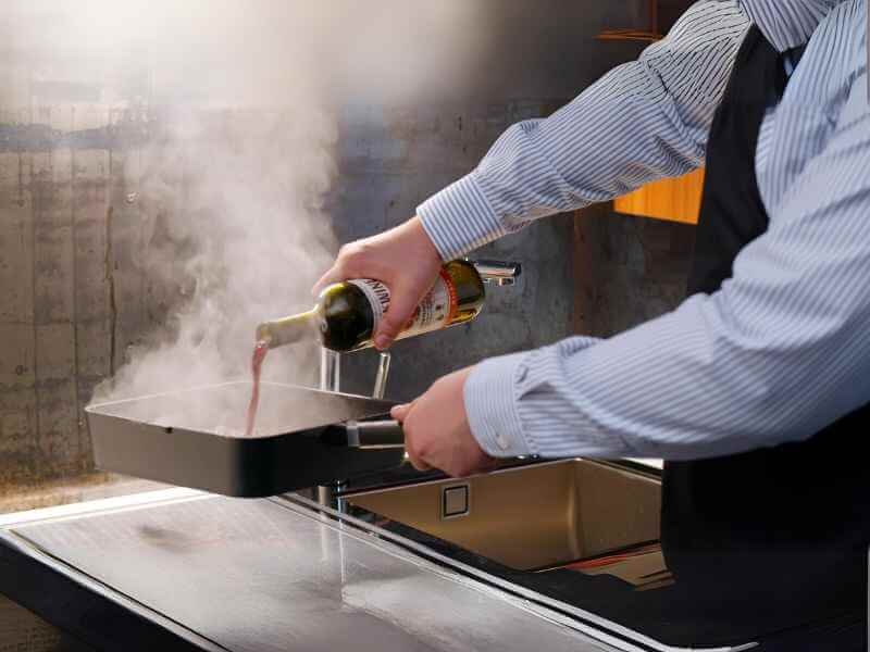 A man is adding wine into the mixture of caramelized onions, garlic tomato paste.